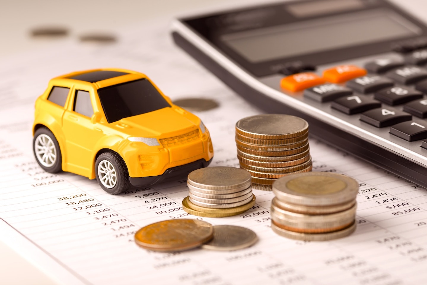 A yellow toy car next to a calculator and some stacks of coins