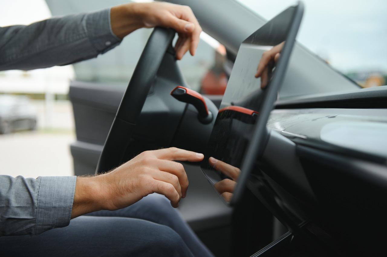 A person inside a car with hands on the steering wheel and dashboard touch pad.